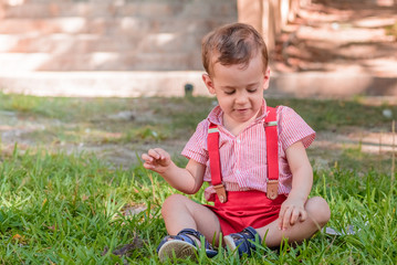 little boy with rjo pants and white shirt sitting on the grass in the park