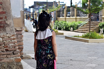 Cute fat little girl watches wedding pictorial on brick wall of old church portal