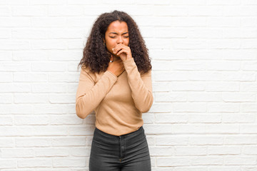 young black woman feeling ill with a sore throat and flu symptoms, coughing with mouth covered...