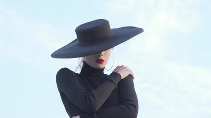 Beautiful mysterious woman in black hugging herself sensually. Stunning female dancer in black outfit practicing her performance outdoors. Seduction, sensuality concept