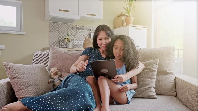 Mother and Daughter having fun on a digital tablet in a home interior. A cute happy mother and daughter using a digital tablet at home in the living room.