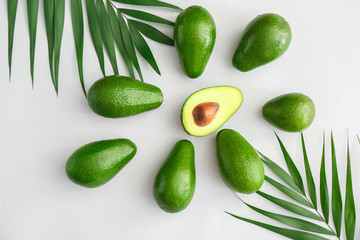 Fresh ripe avocados and palm leaves on white background