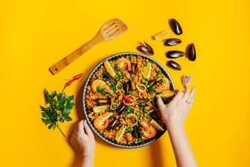 Hands holding pan with spanish paella with seafood on a yellow background