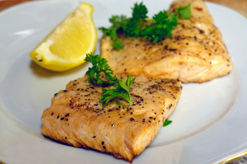 Fried salmon or trout fish fillets with dill and slice of lemon. A beautiful and healthy portion of food on white plate.