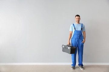 Portrait of handsome plumber with tools box near white wall - obrazy, fototapety, plakaty