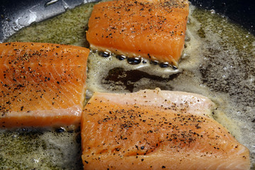 Fototapeta premium Trout fillet steaks on frying pan. Flavored with salt and black pepper.