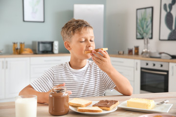 Funny little boy eating tasty toasts with chocolate spreading in kitchen