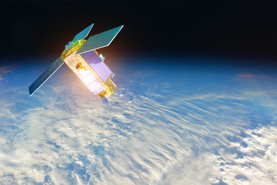 Space satellite at the border of day and night terminator orbiting the earth during sunset and bright rays lights sun reflected from solar panels. Elements of this image furnished by NASA. - Powered by Adobe