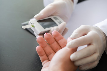 Doctor checking blood sugar level of diabetic patient in clinic, closeup