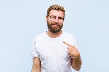 young blonde adult man looking proud, confident and happy, smiling and pointing to self or making...