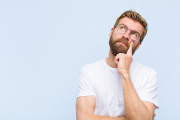 young blonde adult man with a concentrated look, wondering with a doubtful expression, looking up...