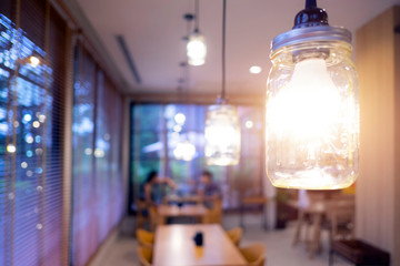 Light bulb hanging in restaurant with dating couple blurred in background. Dinner table in cafe background with shiny light.