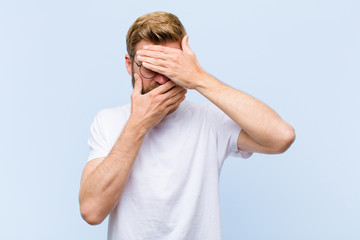 young blonde adult man covering face with both hands saying no to the camera! refusing pictures or...