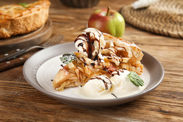Plate with slice of tasty apple pie and ice cream on wooden table