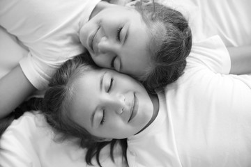 Obraz na płótnie Canvas Black and white portrait of cute twin girls lying on bed, top view