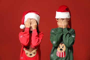 Cute children in Christmas sweaters and Santa hats on color background