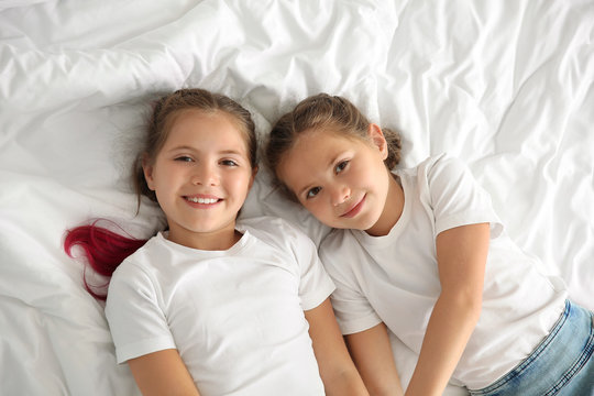 Portrait Of Cute Twin Girls Lying On Bed, Top View