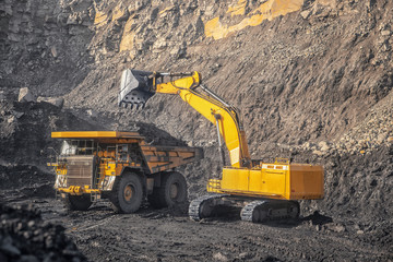 Open pit mine industry, excavator loading coal on big yellow mining truck for anthracite