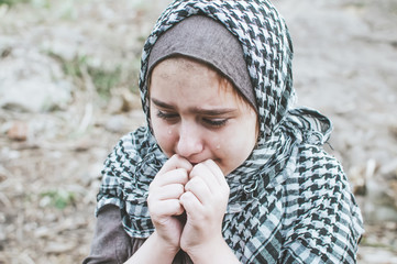 a refugee child in the war, a Muslim girl with a dirty face on the ruins, the concept of peace and war, the child is crying and waiting for help.