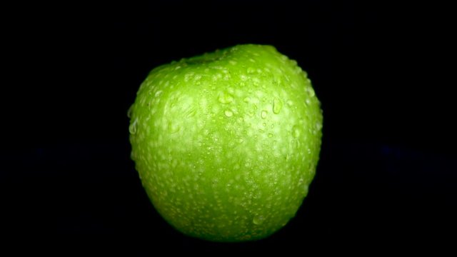 Water is sprayed on a green apple. On a black isolated background. Slow motion