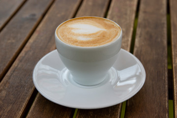 White mug of tasty cappuccino on a wooden table.