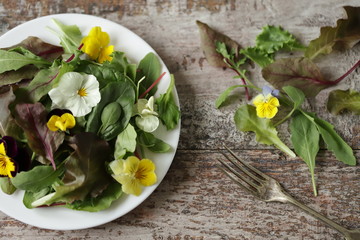 Beautiful mix of salads with flowers on a white plate. Diet concept. Nutrition for girls. Healthy vegan food.