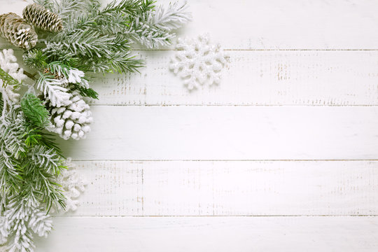 Christmas tree branch with pine cone in snow and retro style clock on a white wooden background. Winter or Christmas festive concept. Flat lay, copy space.