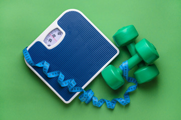 Scales, dumbbells and measuring tape on color background. Weight loss concept