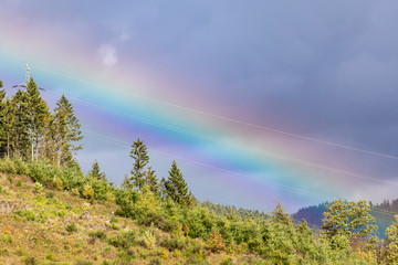 Regenbogen über Bergen mit Stromleitung
