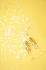 Champagne glasses with gold confetti, glitter yellow background. new year celebration. Top view. The concept of celebration.