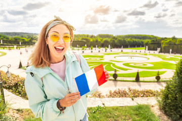 Happy asian woman with french flag travels in Versailles royal garden