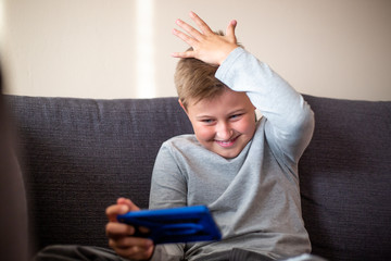 Little cute boy sitting on the sofa and playing games on the mobile