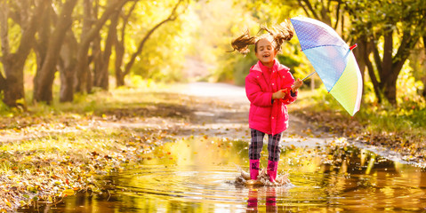 little girl in rubber boots running through a puddle on a rainy day