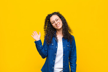young pretty woman smiling happily and cheerfully, waving hand, welcoming and greeting you, or saying goodbye against orange wall © kues1