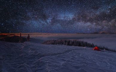 Fairytale landscapes of the winter Carpathian Mountains with a charming milky way in the sky tourist tents and snowy houses in the valleys