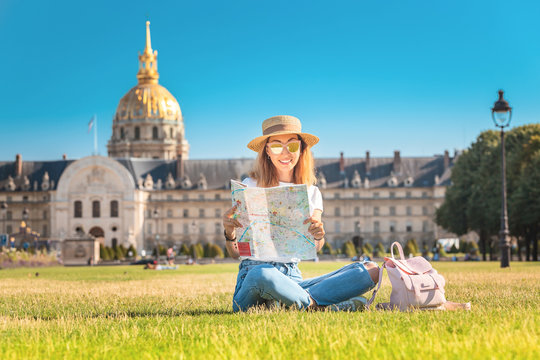 Asian happy girl traveler lying on a grass and reading map near the Invalides In Paris. Lifestyle and tourism in France