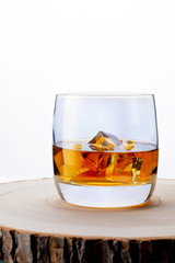 Glass of whiskey with ice on a wooden board. Wooden saw cut. White background. Whiskey / Brandy / Cognac / Rum. Glass with a strong drink.