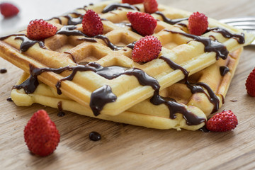 Two Viennese waffles with chocolate and berries on a wooden Board