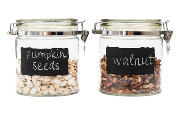Pumpkin seeds and walnuts in a glass jars, flip-top closure, isolated on white background