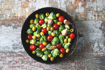Brussels sprouts in a pan with cherry tomatoes, garlic and olives before baking. Healthy food. Vegan diet. Vegetable pan.