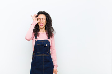 young pretty woman smiling happily with funny face, joking and looking through peephole, spying on...