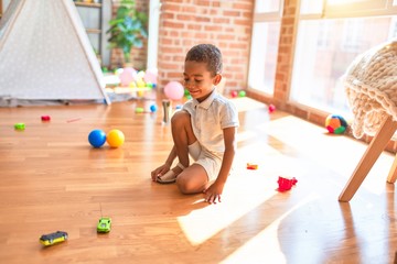 Beautiful african american toddler playing with cars around lots of toys at kindergarten