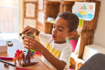Beautiful african american toddler playing with dinosaurs toy on desk at kindergarten