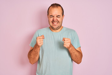 Young man wearing blue casual t-shirt standing over isolated pink background excited for success with arms raised and eyes closed celebrating victory smiling. Winner concept.