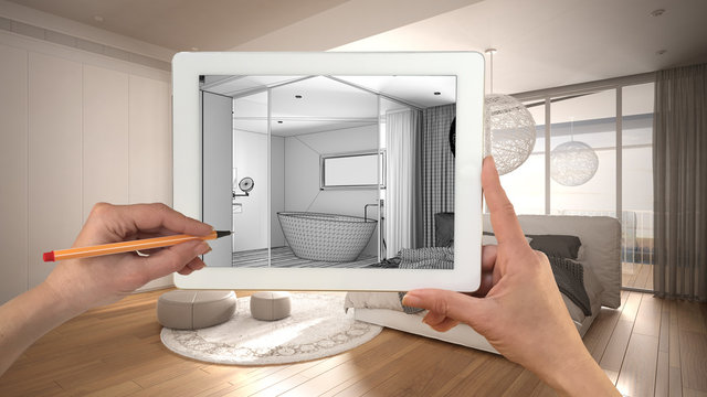 Hands holding and drawing on tablet showing modern white bedroom with bathroom details CAD sketch. Real finished interior in the background, architecture design presentation