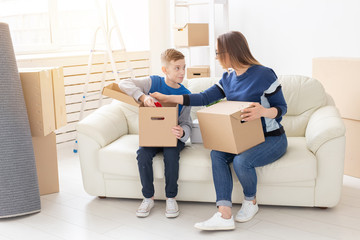 Cute single mom and little boy son sort boxes with things after the move. The concept of housewarming mortgage and the joy of new housing.