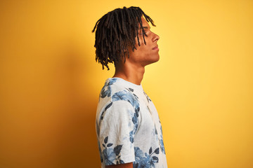 Afro man with dreadlocks wearing summer floral t-shirt over isolated yellow background looking to side, relax profile pose with natural face with confident smile.