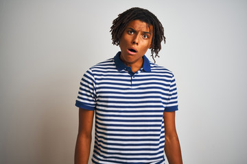 Afro man with dreadlocks wearing striped blue polo standing over isolated white background In shock face, looking skeptical and sarcastic, surprised with open mouth