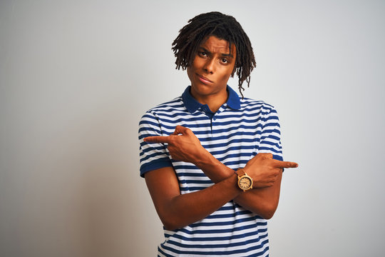 Afro man with dreadlocks wearing striped blue polo standing over isolated white background Pointing to both sides with fingers, different direction disagree