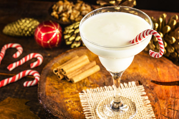 Eggnog in glass with various ingredients, food and Christmas decorative objects in the background, Christmas balls, panettone, cinnamon and golden pines. Drink for Christmas dinner. Selective focus.